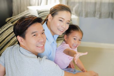 Mutlu Asyalı aile oturma odasındaki kanepede tablet izliyor.