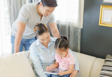 Mutlu Asyalı aile oturma odasındaki kanepede tablet izliyor.