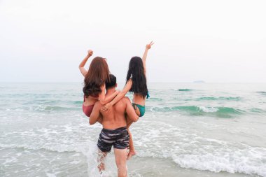 Asyalı yakışıklı adam sahilde bikini giyen kadınları taşıyor.