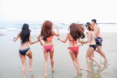Soyut, bulanık, seksi bikinili, mayo giyen Asyalı kadınlar sahilde arkadaşlarıyla oynuyorlar.