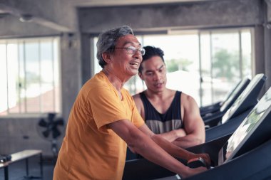 Asyalı son sınıf öğrencisi ve antrenör spor salonunda koşu bandında egzersiz yapıyor.