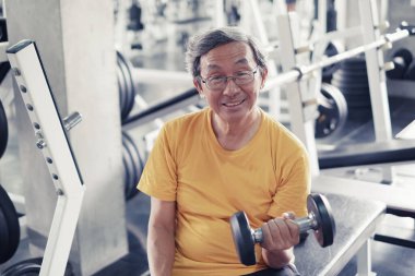 Portre Asyalı yaşlı adam spor yapıyor ya da spor yapıyor ya da spor yapıyor. Ya da spor salonunda küçük bir halter, güçlü bir spor ve sağlıklı bir konsept kullanıyor.