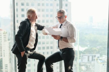 İki kıdemli iş adamı, birlikte çalışmak için gökdelen ya da ofiste buluşuyor.