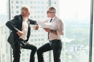 İki kıdemli iş adamı, birlikte çalışmak için gökdelen ya da ofiste buluşuyor.