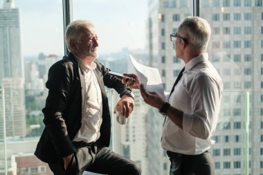İki kıdemli iş adamı, birlikte çalışmak için gökdelen ya da ofiste buluşuyor.