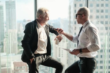 İki kıdemli iş adamı, birlikte çalışmak için gökdelen ya da ofiste buluşuyor.