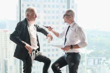 İki kıdemli iş adamı, birlikte çalışmak için gökdelen ya da ofiste buluşuyor.
