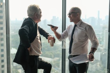 İki kıdemli iş adamı, birlikte çalışmak için gökdelen ya da ofiste buluşuyor.