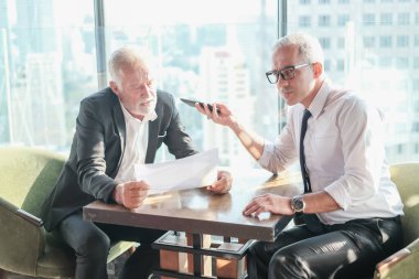 İki kıdemli iş adamı, birlikte çalışmak için gökdelen ya da ofiste buluşuyor.