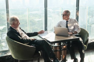 İki kıdemli iş adamı, birlikte çalışmak için gökdelen ya da ofiste buluşuyor.