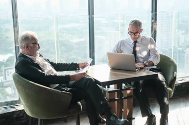 İki kıdemli iş adamı, birlikte çalışmak için gökdelen ya da ofiste buluşuyor.