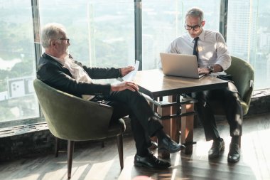 İki kıdemli iş adamı, birlikte çalışmak için gökdelen ya da ofiste buluşuyor.