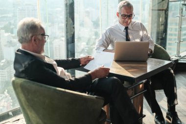 İki kıdemli iş adamı, birlikte çalışmak için gökdelen ya da ofiste buluşuyor.