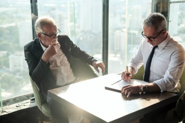 İki kıdemli iş adamı, birlikte çalışmak için gökdelen ya da ofiste buluşuyor.