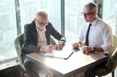 İki kıdemli iş adamı, birlikte çalışmak için gökdelen ya da ofiste buluşuyor.