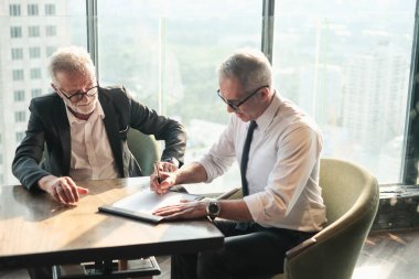 İki kıdemli iş adamı, birlikte çalışmak için gökdelen ya da ofiste buluşuyor.