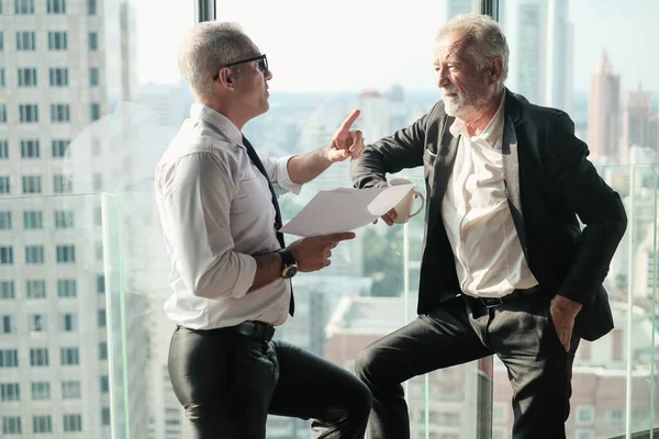 İki kıdemli iş adamı, birlikte çalışmak için gökdelen ya da ofiste buluşuyor.