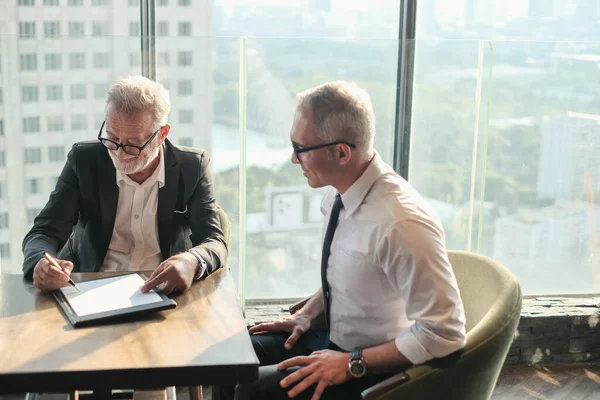 İki kıdemli iş adamı, birlikte çalışmak için gökdelen ya da ofiste buluşuyor.