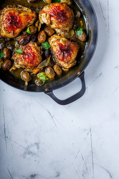 Siyah tavada tavuk ve zeytin soslu ve otlu beyaz arka planda.