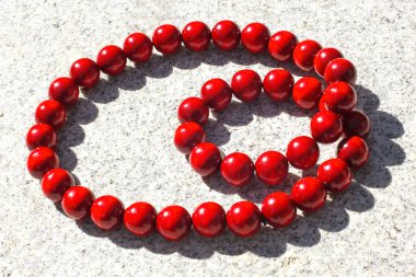 Büyük kırmızı ahşap boncuklar, gri arka planda güneş tarafından aydınlatılıyor.