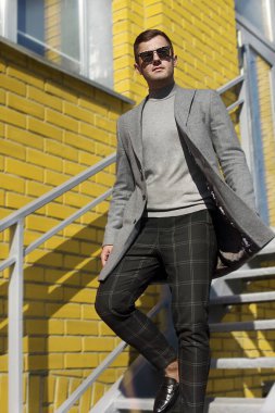 Gri paltolu bir adam merdivenlerden iniyor. Erkekler için dış giyim reklamı..