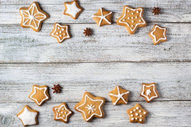 Beyaz ahşap bir arka planda parıltı ve baharat desenleri olan bir yıldız şeklinde Noel zencefilli ekmek sınırı. Kopyalama alanı olan üst görünüm