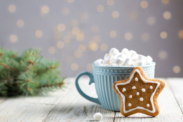 Голубая чашка зимнего горячего напитка с зефиром и пряничной звездой на белом деревянном фоне. Традиционная рождественская атмосфера с боке. Новогодний праздник. Праздничный фон