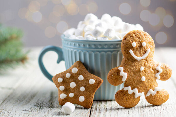 Голубая чашка зимнего горячего напитка с зефиром и пряничным печеньем на белом деревянном фоне. Праздничный рождественский фон. Традиционная рождественская атмосфера с боке. Новогодний праздник.