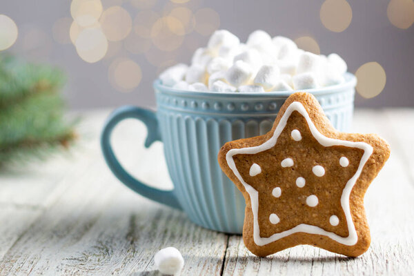 Голубая чашка зимнего горячего напитка с зефиром и пряничной звездой на белом деревянном фоне. Традиционная рождественская атмосфера с боке. Новогодний праздник. Праздничный фон