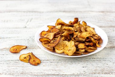 Ahşap arka planda beyaz bir tabakta dilimlenmiş kuru armut yığını. Kurutulmuş meyve cipsi. Sağlıklı vejetaryen yemekleri.