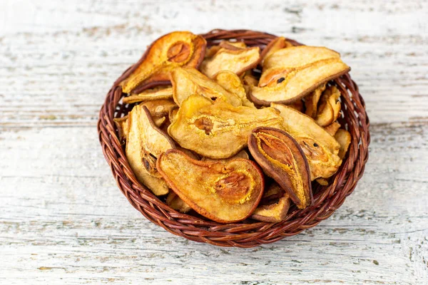 Beyaz ahşap arka planda hasır sepette kurumuş armut dilimleri yığını. Kurutulmuş meyve cipsi. Sağlıklı yiyecekler. Üst görünüm