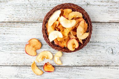 Hasır sepette beyaz ahşap arka planda kurumuş elma dilimleri yığını. Kurutulmuş meyve cipsi. Sağlıklı yiyecekler. Üst görünüm