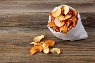 Ahşap arka plandaki beyaz bir keseden alınmış kurumuş elma hapları yığını. Kurutulmuş meyve cipsi. Sağlıklı vejetaryen yemekleri