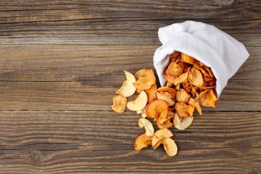 Ahşap arka plandaki beyaz bir keseden alınmış kurumuş elma hapları yığını. Kurutulmuş meyve cipsi. Sağlıklı vejetaryen yemekleri