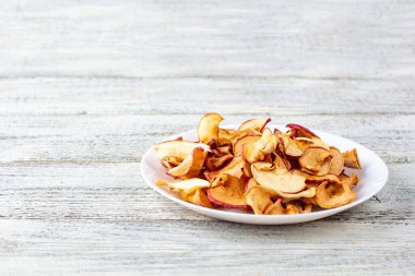 Ahşap arka planda beyaz bir tabakta dilimlenmiş bir yığın kuru elma. Kurutulmuş meyve cipsi. Sağlıklı vejetaryen yemekleri