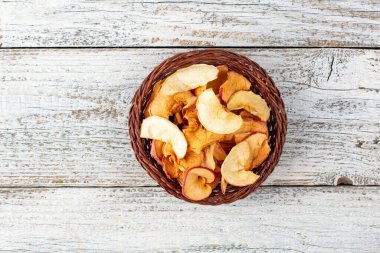 Hasır sepette beyaz ahşap arka planda kurumuş elma dilimleri yığını. Kurutulmuş meyve cipsi. Sağlıklı yiyecekler. Kopyalama alanı olan üst görünüm