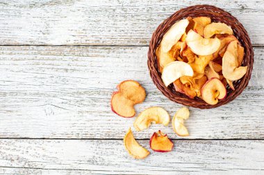 Hasır sepette beyaz ahşap arka planda kurumuş elma dilimleri yığını. Kurutulmuş meyve cipsi. Sağlıklı yiyecekler. Kopyalama alanı olan üst görünüm
