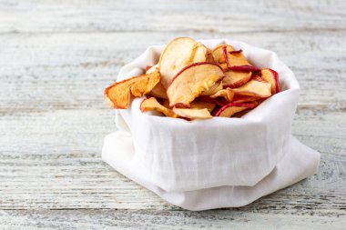 Ahşap arka planda beyaz kesede kurumuş elma dilimleri yığını. Kurutulmuş meyve cipsi. Sağlıklı vejetaryen yemekleri