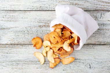 Ahşap arka plandaki beyaz bir keseden alınmış kurumuş elma hapları yığını. Kurutulmuş meyve cipsi. Sağlıklı vejetaryen yemekleri