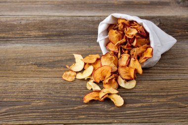 Ahşap arka plandaki beyaz bir keseden alınmış kurumuş elma hapları yığını. Kurutulmuş meyve cipsi. Sağlıklı vejetaryen yemekleri