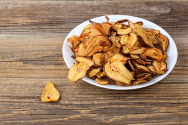 Ahşap arka planda beyaz bir tabakta dilimlenmiş kuru armut yığını. Kurutulmuş meyve cipsi. Sağlıklı vejetaryen yemekleri