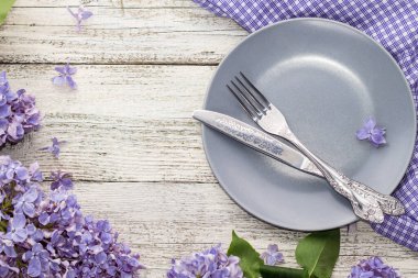 Tabak çatalı ve beyaz ahşap arka planda leylak çiçekleriyle süslenmiş bıçak ile servis masası. 2022 yılının modaya uygun renginde fotokopi alanı olan üst görünüm. 2022 Yılı Rengi.