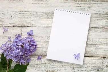 Beyaz ahşap arka planda bahar leylağı çiçekleri olan temiz bir not defteri. 2022 'nin modaya uygun renginde telif alanı olan üst görünüm. 2022 Yılı Rengi.