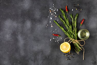 Koyu taş zemin üzerinde biber, tuz, limon ve yağ ile bir demet yeşil biberiye. Tarifler için baharat ve bitkiler. Kopyalama alanı olan üst görünüm.