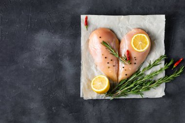 Biberiyeli kalp şeklinde çiğ tavuk filetosu ve koyu beton arka planda baharatlar. Kopyalama alanı olan üst görünüm