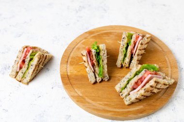 Salamlı, peynirli, domatesli, salatalı, soğanlı sandviç. Beyaz arka planda tahıl ekmeği olan klasik kulüp sandviçi..