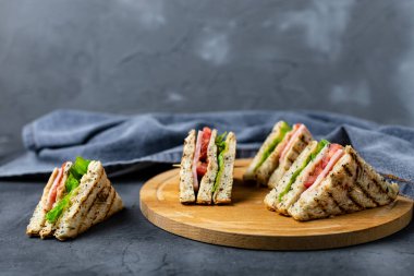 Salamlı, peynirli, domatesli, salatalı, soğanlı sandviç. Koyu arkaplanda tahıl ekmeği olan klasik kulüp sandviçi..