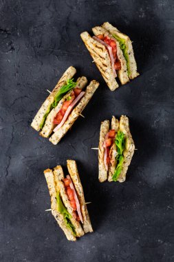 Jambonlu, peynirli, domatesli, salatalı, soğanlı sandviç. Koyu arkaplanda tahıl ekmeği olan klasik kulüp sandviçi..