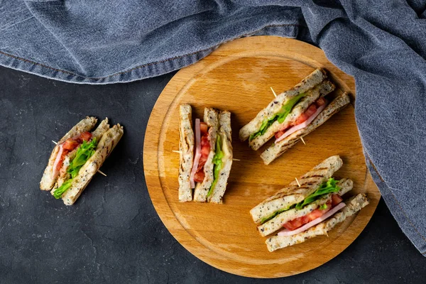 Salamlı, peynirli, domatesli, salatalı, soğanlı sandviç. Koyu arkaplanda tahıl ekmeği olan klasik kulüp sandviçi..