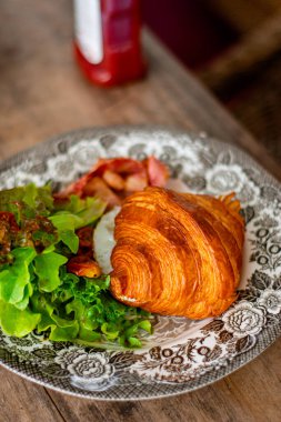 Çırpılmış yumurta ve kızarmış pastırmalı kruvasan sandviçi kahvaltısı..